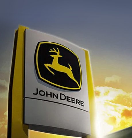 Ein Schild mit dem John Deere Logo steht vor einem Gebäude und im Hintergrund geht die Sonne unter.