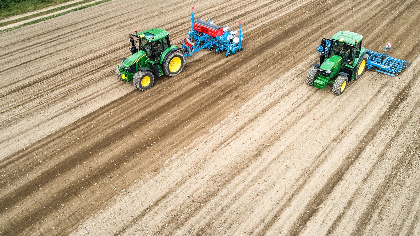 Zwei 6M-Traktoren von John Deere auf einem unbearbeiteten Feld. Einer davon zieht eine Einzelkorns&auml;maschine von Monsomen.  Der andere zieht eine Saatbettkombination von Lemken.