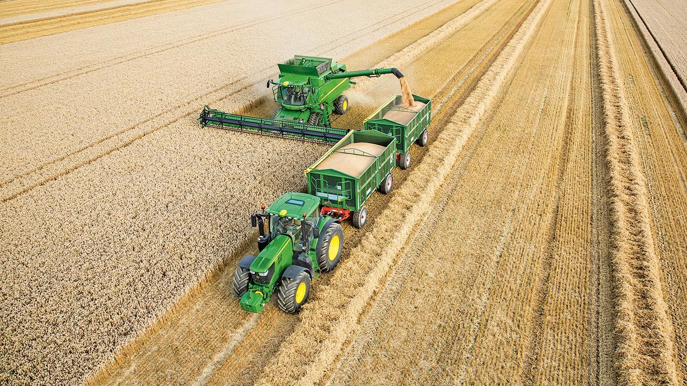 Der John Deere M&auml;hdrescher der S-Serie entl&auml;dt Weizen in zwei Anh&auml;nger, die vom Traktor gezogen werden