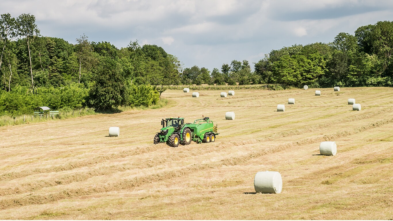 John Deere Traktor mit Ballenpresse auf einem Feld mit Silageballen