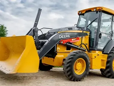 Elektrischer Baggerlader John Deere 310 X-Tier auf einer Schotterstraße.